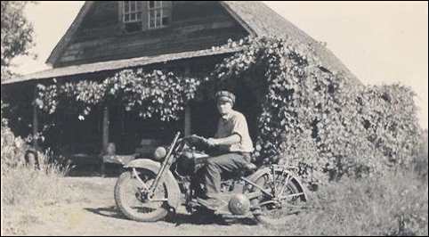 Celian Adams on Harley by log house in Mosquito - 1940